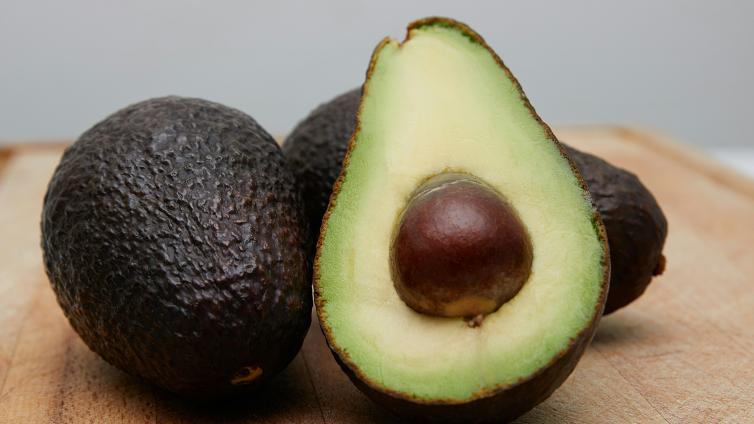 Avocado slides in half resting on other full avocados