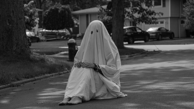 Person in a ghost costume sitting alone in the street